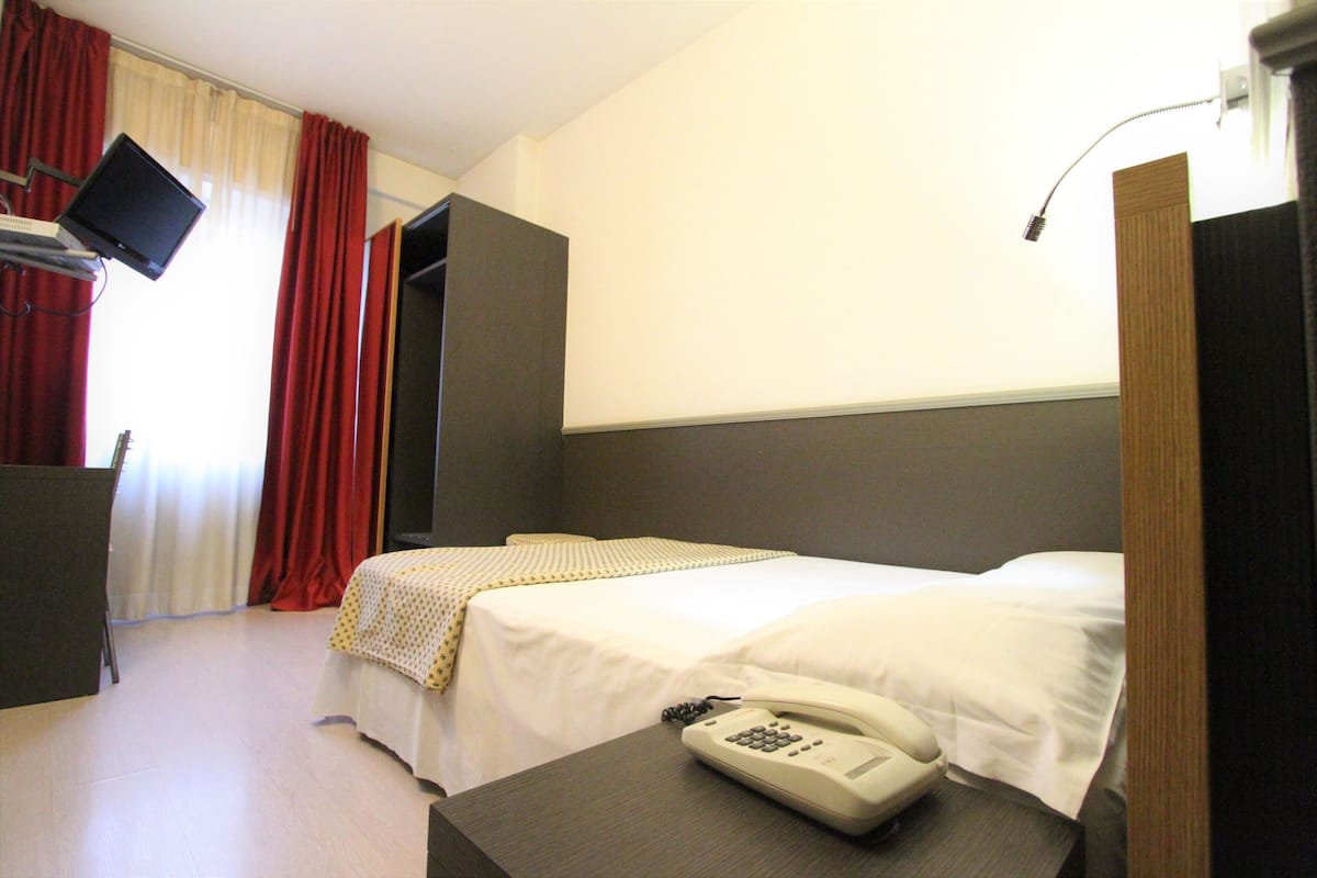 A hotel room with a bed, a bedside telephone, a television on a stand, and a wardrobe.