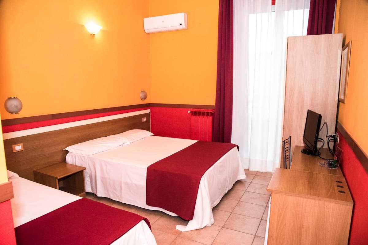 A hotel room with two beds, a desk with a computer, a mirror, and a red and white color scheme.
