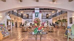 A spacious lobby with a central glass table surrounded by wicker furniture, a staircase, and a Christmas tree.