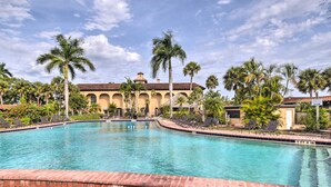 A swimming pool with lounge chairs and palm trees, surrounded by a building with a tiled roof.