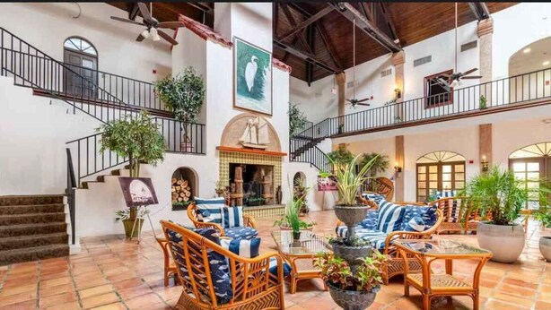 A spacious indoor area with a high ceiling, a staircase, wicker furniture, and potted plants.