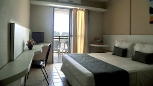 A hotel room with a bed, a desk with a chair, a television, and a window with curtains. - Costa Do Atlantico (Natal)
