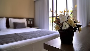 A hotel room with a bed, a bedside table with a vase of flowers, and a window with curtains. - Costa Do Atlantico (Natal)
