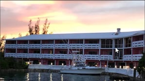 A large building with multiple balconies, a boat docked in front, and a calm body of water reflecting the sky. - Bell Channel Inn Hotel (Freeport)