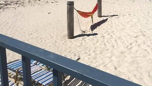 A beach with a wooden fence and a hammock. There are striped lounge chairs in the foreground. - Bell Channel Inn Hotel (Freeport)