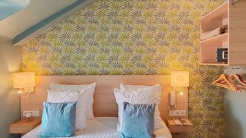 Una habitación de hotel con cama, dos mesitas de noche, un tocador, un estante en la pared y un perchero.