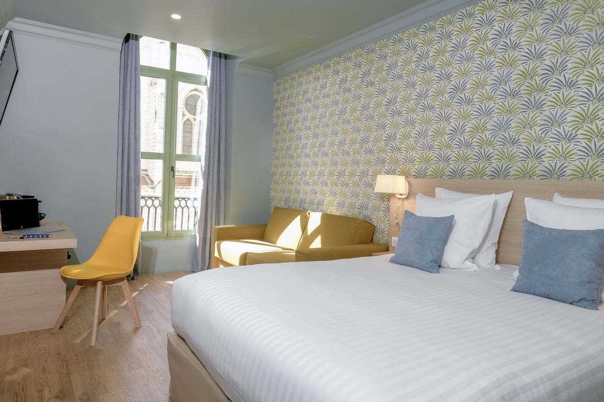 A hotel room with a bed, a desk, a chair, and a window with curtains.