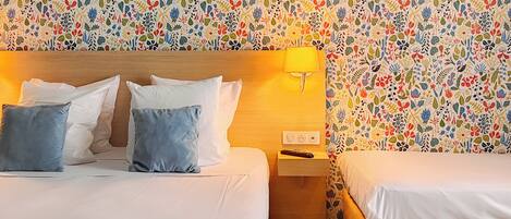 A hotel room with two beds, a wooden headboard, a nightstand, and a wall with a floral pattern.