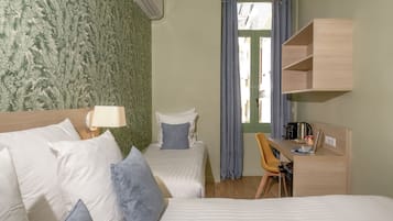A hotel room with two beds, a desk with a chair, a window with curtains, and a wall-mounted shelf.