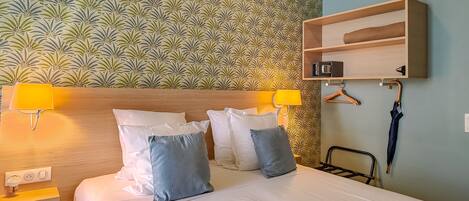 Une chambre d’hôtel avec un lit, deux lampes de chevet, une tête de lit en bois, une étagère fixée au mur et un parapluie suspendu.