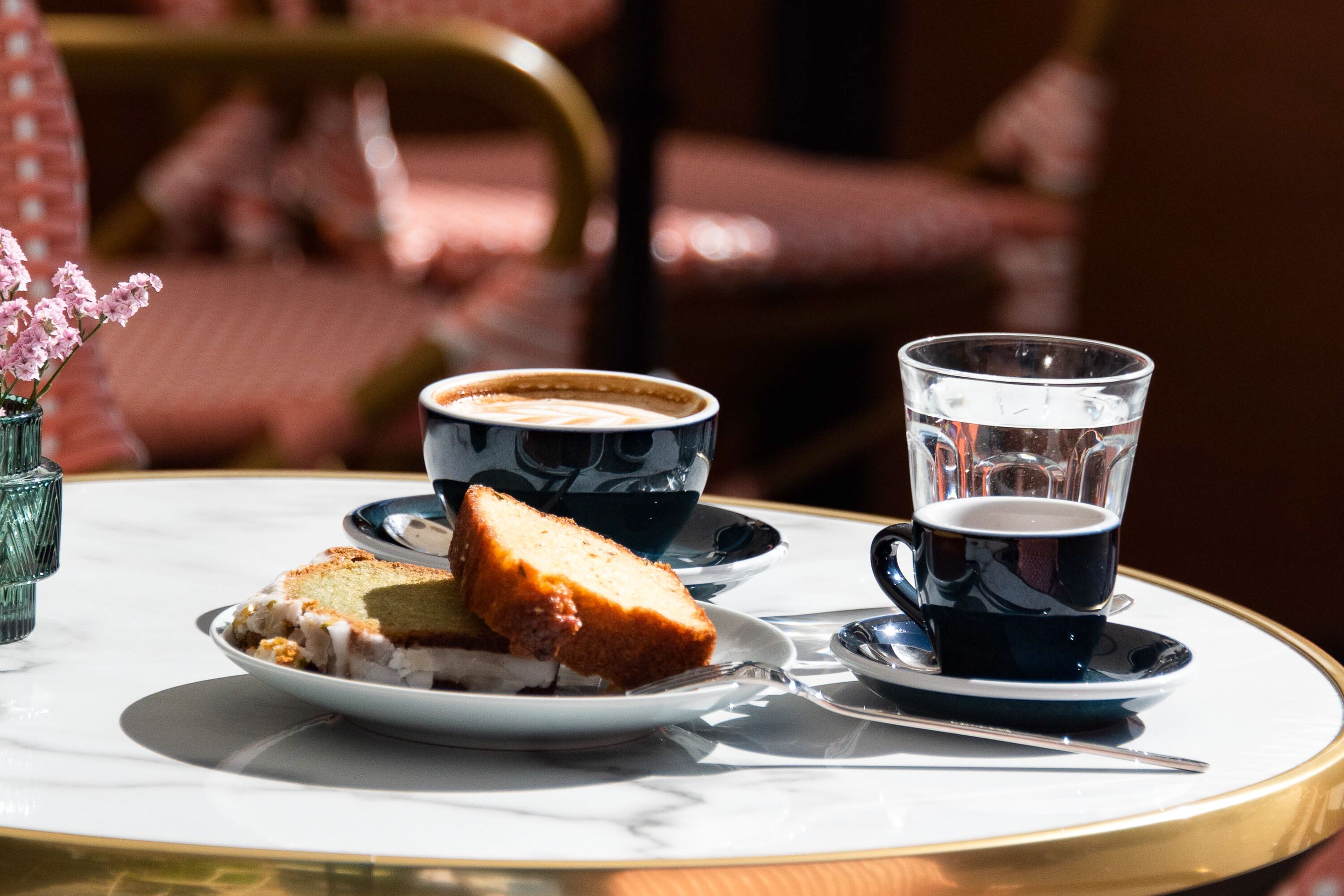 Une table avec une tasse de café, un verre d’eau et une assiette contenant un sandwich.