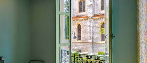 A room with a view of a historic building through a window with a decorative iron railing.