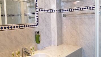 Un baño con un lavamanos blanco, un espejo, cabina de ducha de cristal y un perchero para toallas.