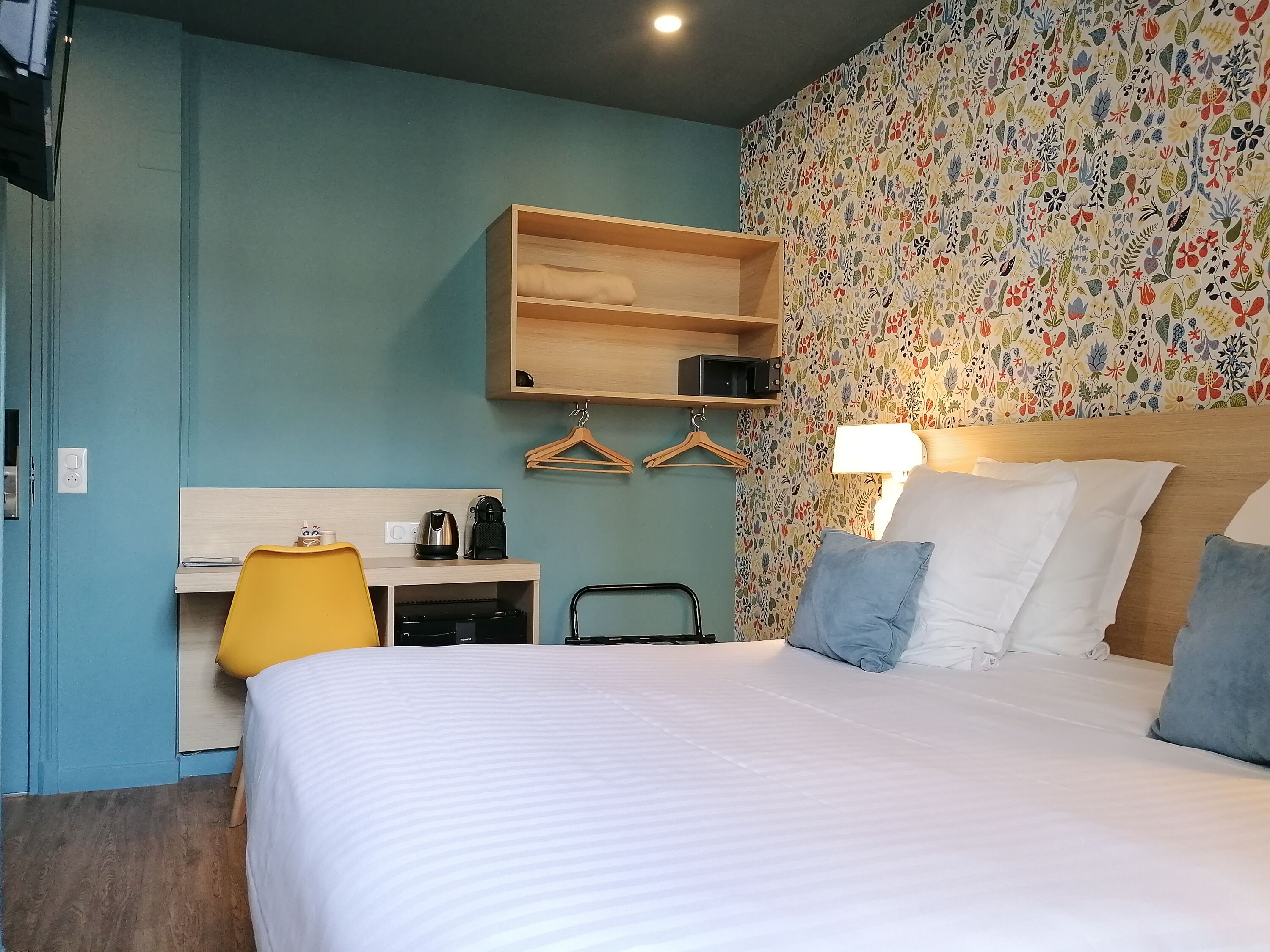 Une chambre d’hôtel comprenant un lit, un bureau avec une bouilloire, une lampe et une armoire.