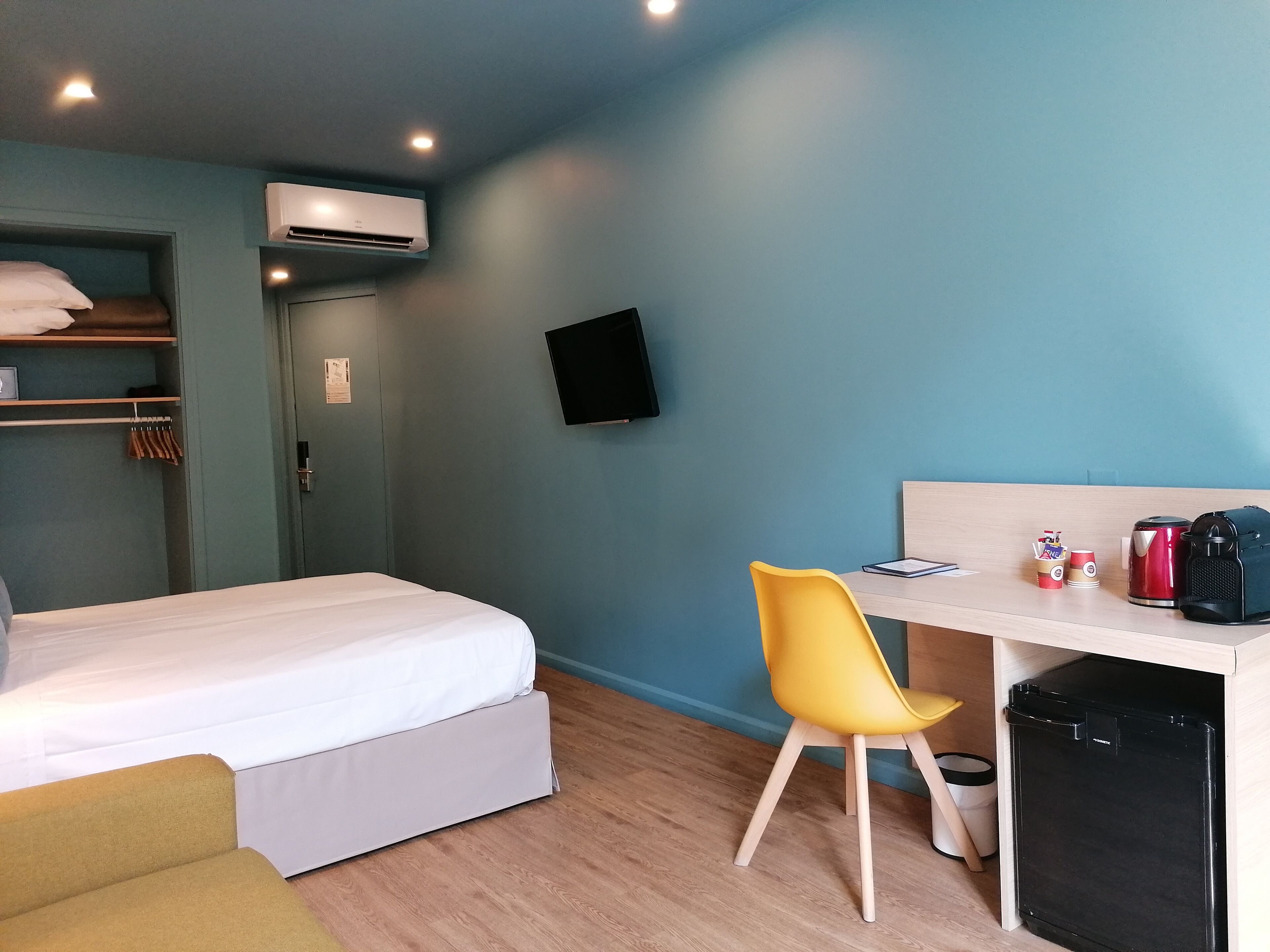 A hotel room with a bed, a desk with a chair, a TV, a mini fridge, and a trash bin.