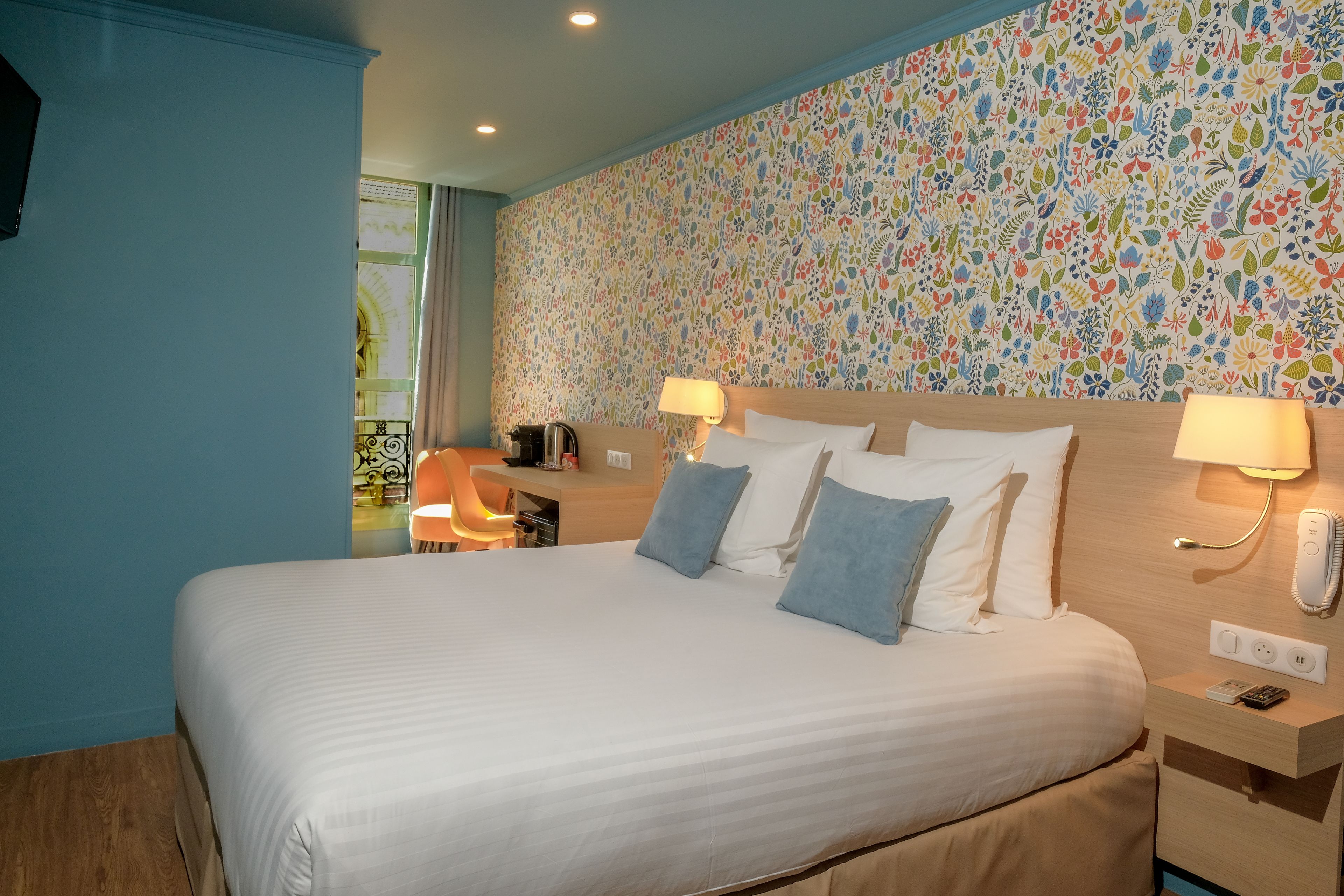 Een hotelkamer met een groot bed, twee bedlampen, een nachtkastje en een wand met bloemenpatroon.