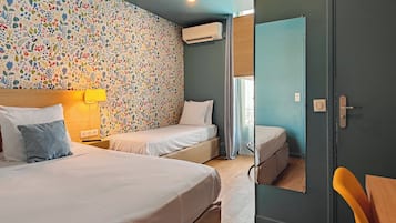 A hotel room with two beds, a colorful floral wall, an air conditioning unit, and a wooden door.