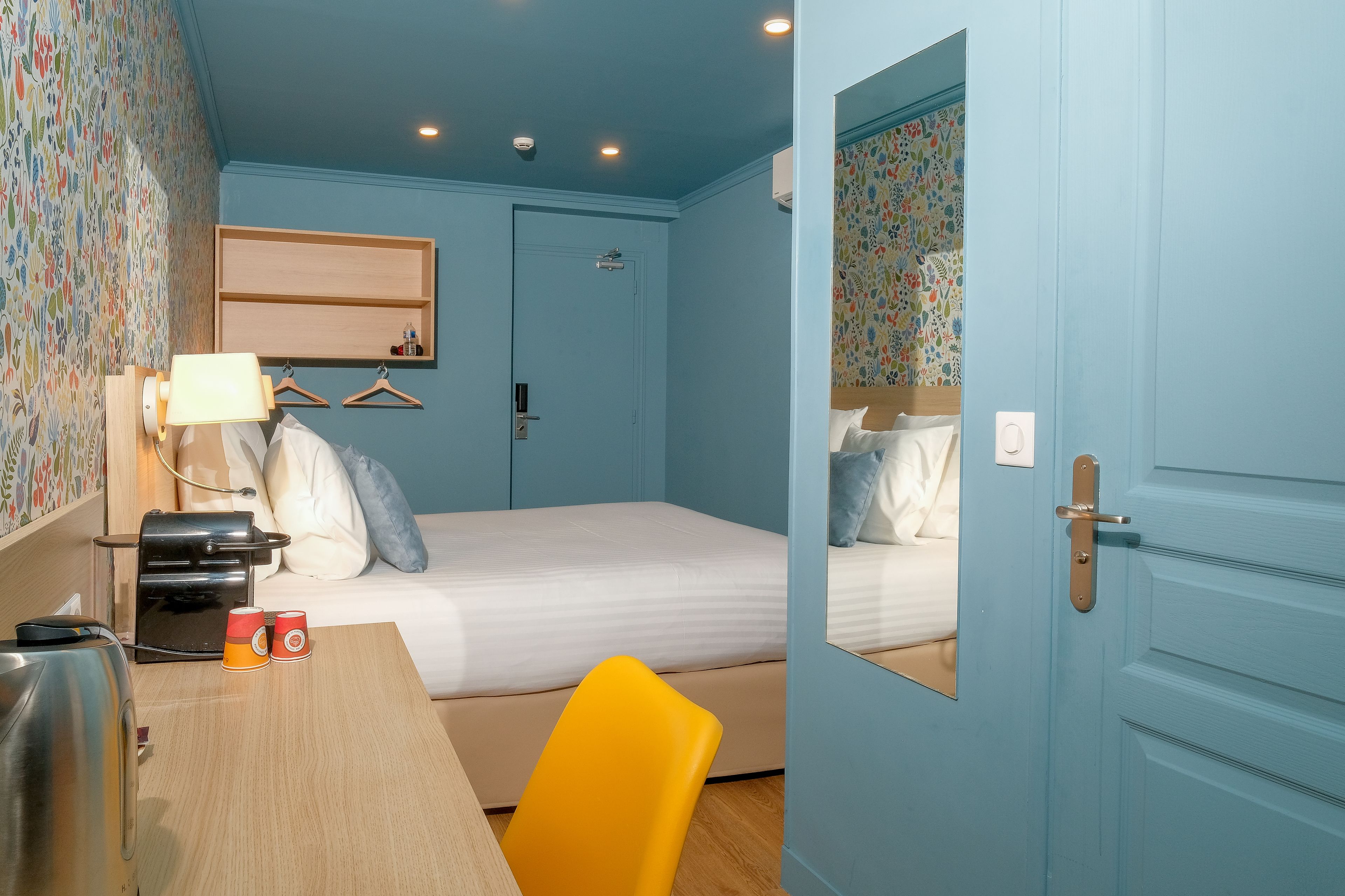 A bedroom with a bed, a desk with a lamp, a chair, and a mirror.