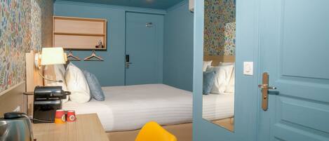A bedroom with a bed, a desk with a lamp, a chair, and a mirror.