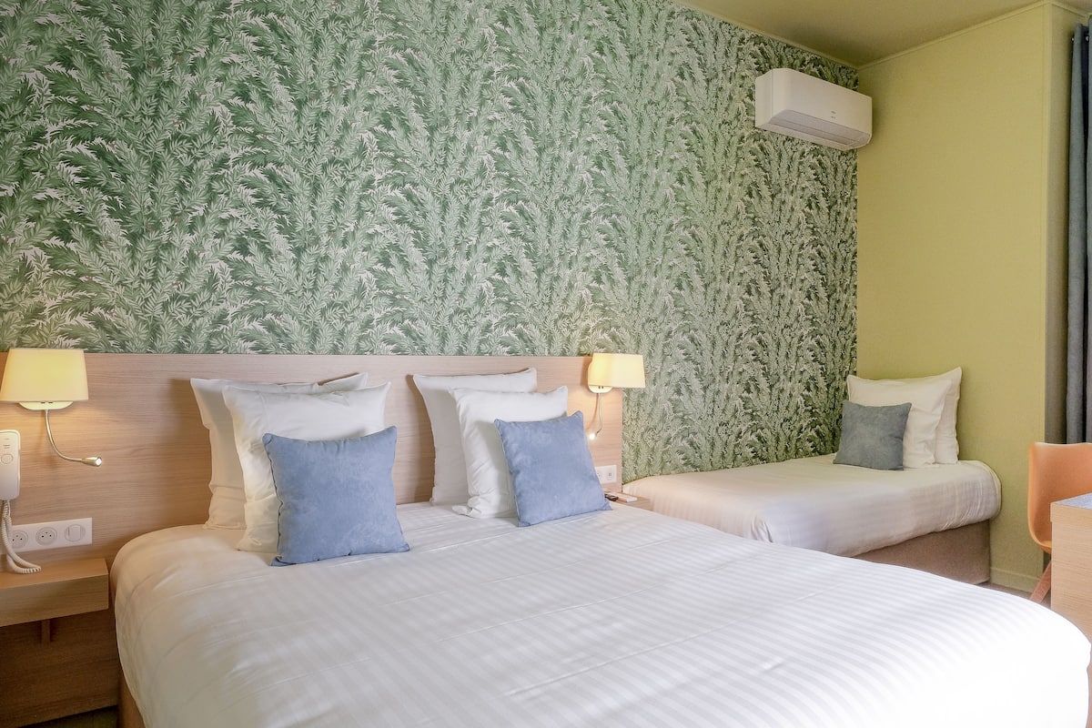 A hotel room with two beds, a green textured wall, and an air conditioning unit.