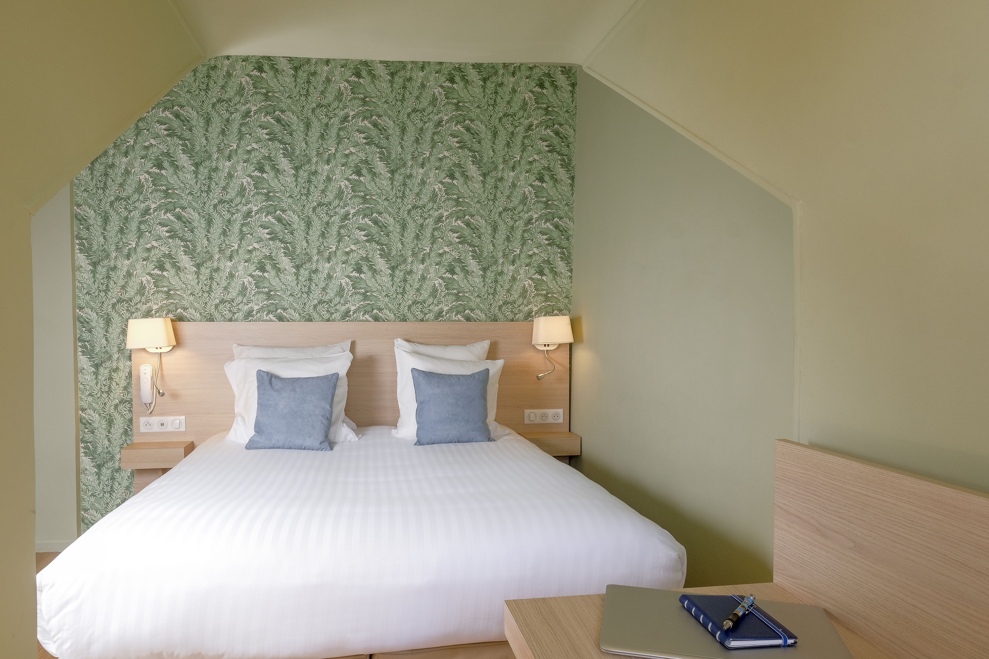 A hotel room with a bed, two bedside lamps, a nightstand, a laptop, and a notebook.