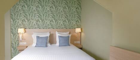 A hotel room with a bed, two bedside lamps, a nightstand, a laptop, and a notebook.