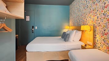 Ett hotellrum med två sängar, en garderob i trä, en vägg med ett blommönster och en dörr med lås.