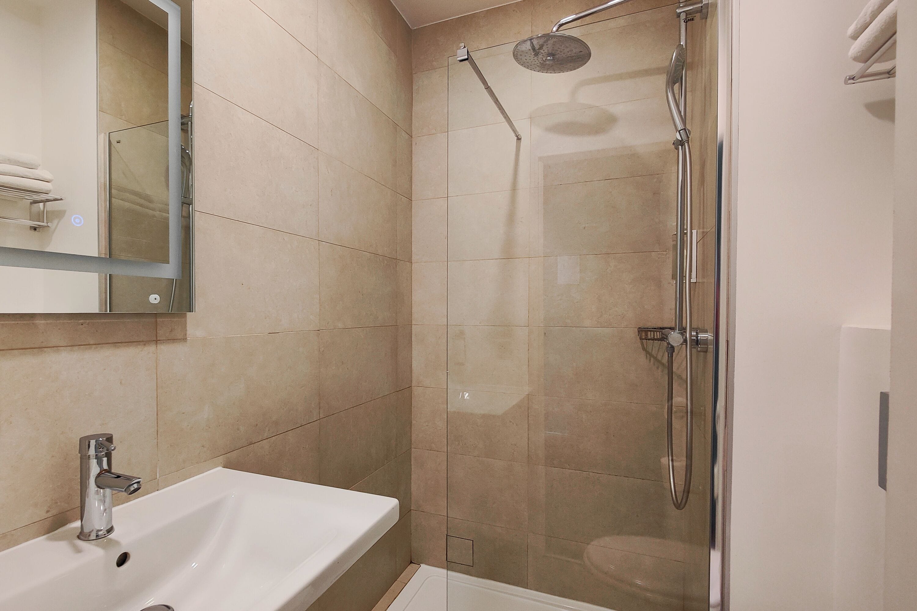 Un baño moderno con ducha de vidrio, un lavabo blanco y un espejo sobre él.
