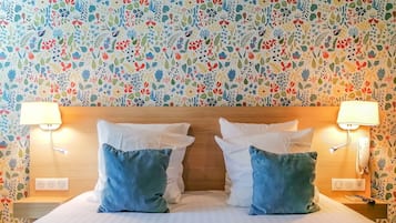 Ein Hotelzimmer mit floralem Wandpapier, einem hölzernen Kopfteil, zwei Nachttischlampen und einem Bett mit weißen und blauen Kissen.