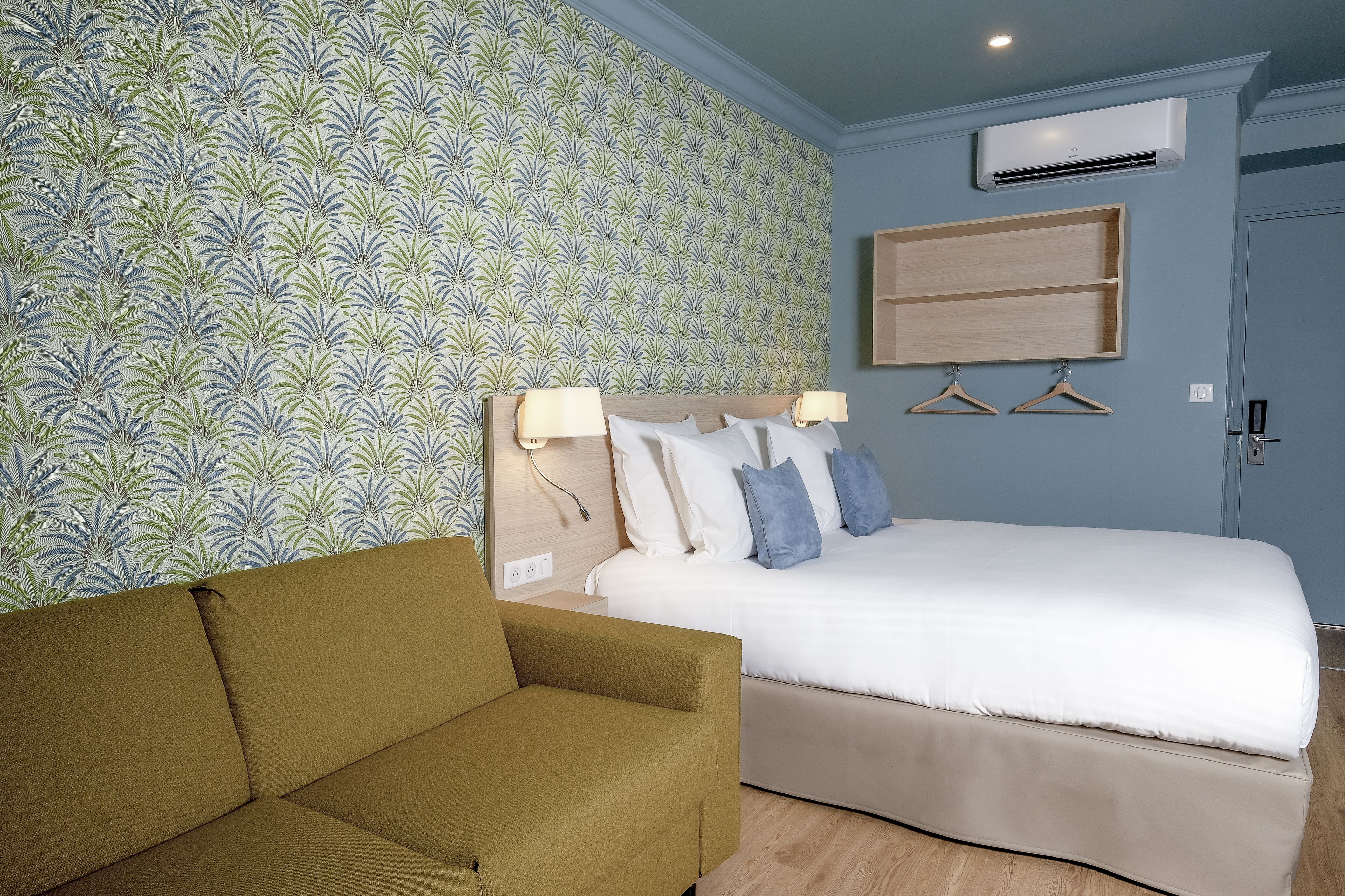 Une chambre d’hôtel comprenant un lit, un canapé, une étagère fixée au mur et une armoire.
