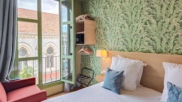 Een hotelkamer met een bed, een stoel, een kledingkast en een raam met uitzicht op een gebouw.