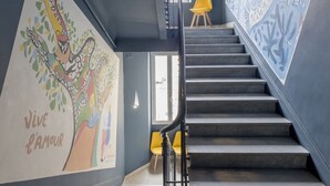 A staircase with a hand-painted mural on the wall, a yellow chair, and a modern light fixture. - Hotel Du Centre, un hotel AMMI (Nice)