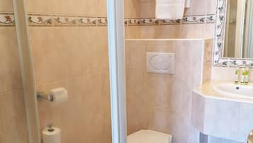 A bathroom with a glass shower enclosure, a toilet, a sink with toiletries, and a mirror with floral tiles.
