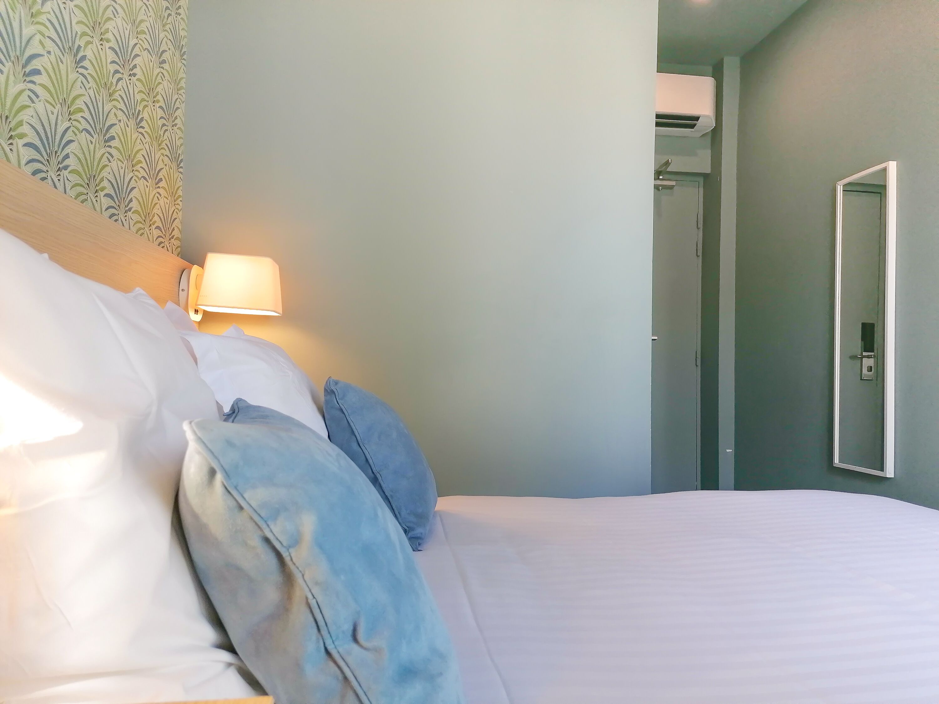 Ein Hotelzimmer mit Bett, Kissen, einer Nachttischlampe und einem Spiegel.