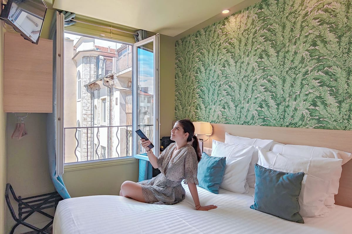A room with a bed, a window, a wall with a leafy pattern, and a chair.