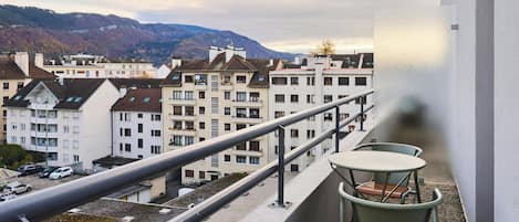 Un balcón con mesa y sillas, con vista a una zona residencial con varios edificios y una montaña al fondo.