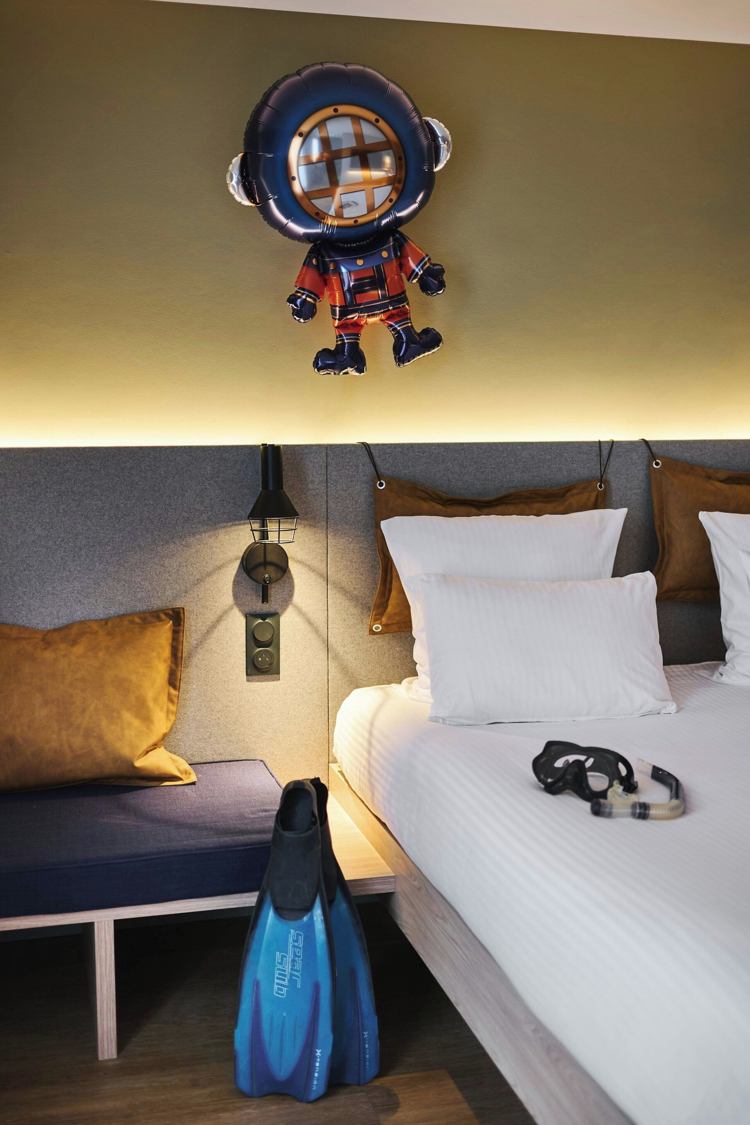 A hotel room with a bed, pillows, a nightstand, a lamp, and a diver's gear on the floor.