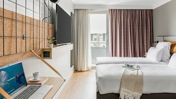 Quarto de hotel moderno com uma cama grande, uma escrivaninha com um laptop, uma televisão de tela plana na parede e uma varanda com cortinas.