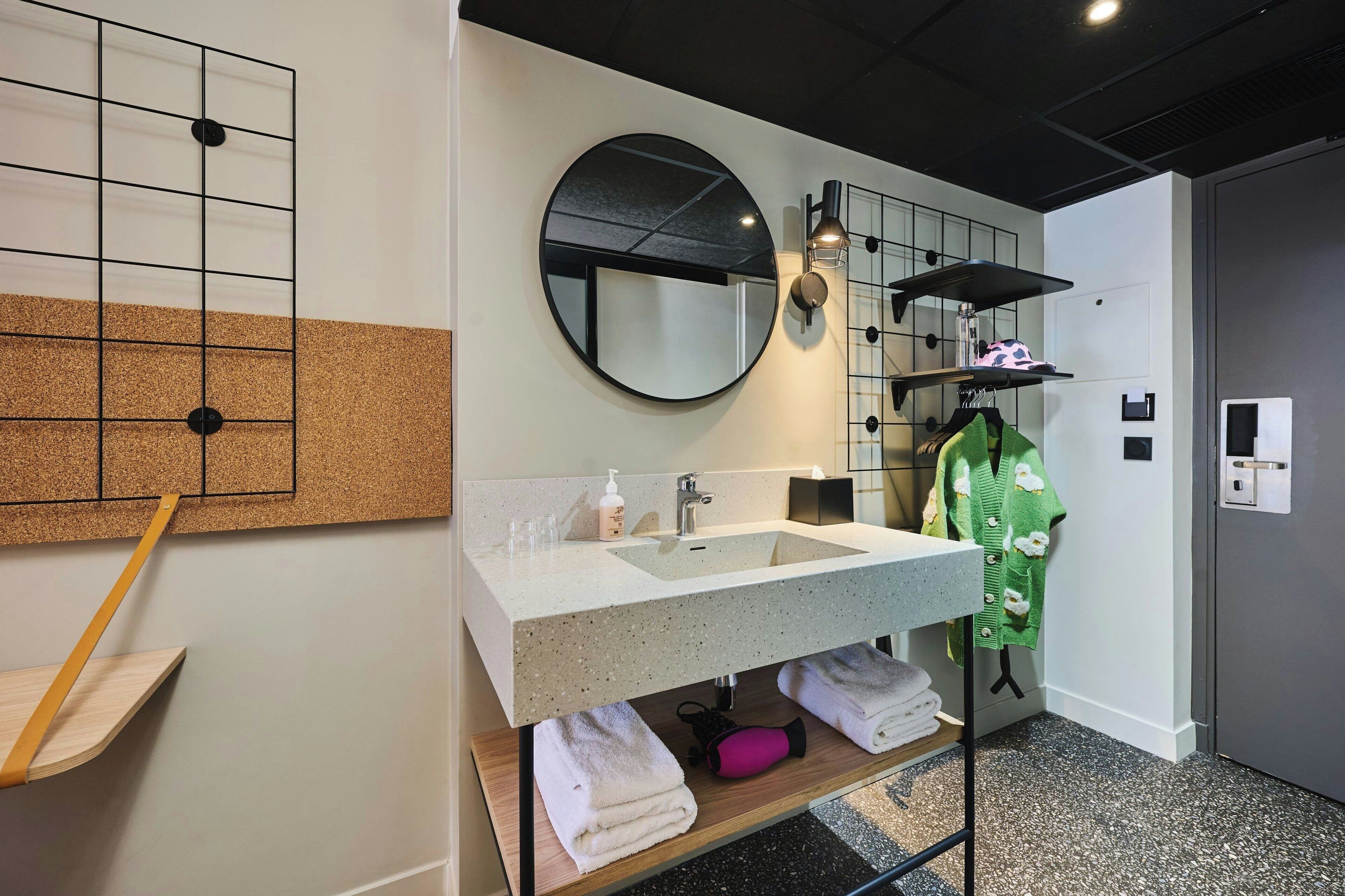 Een moderne badkamer met een ruime wastafel, spiegel, handdoekhouder en een prikbordwand.