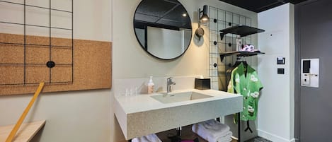 Een moderne badkamer met een ruime wastafel, spiegel, handdoekhouder en een prikbordwand.
