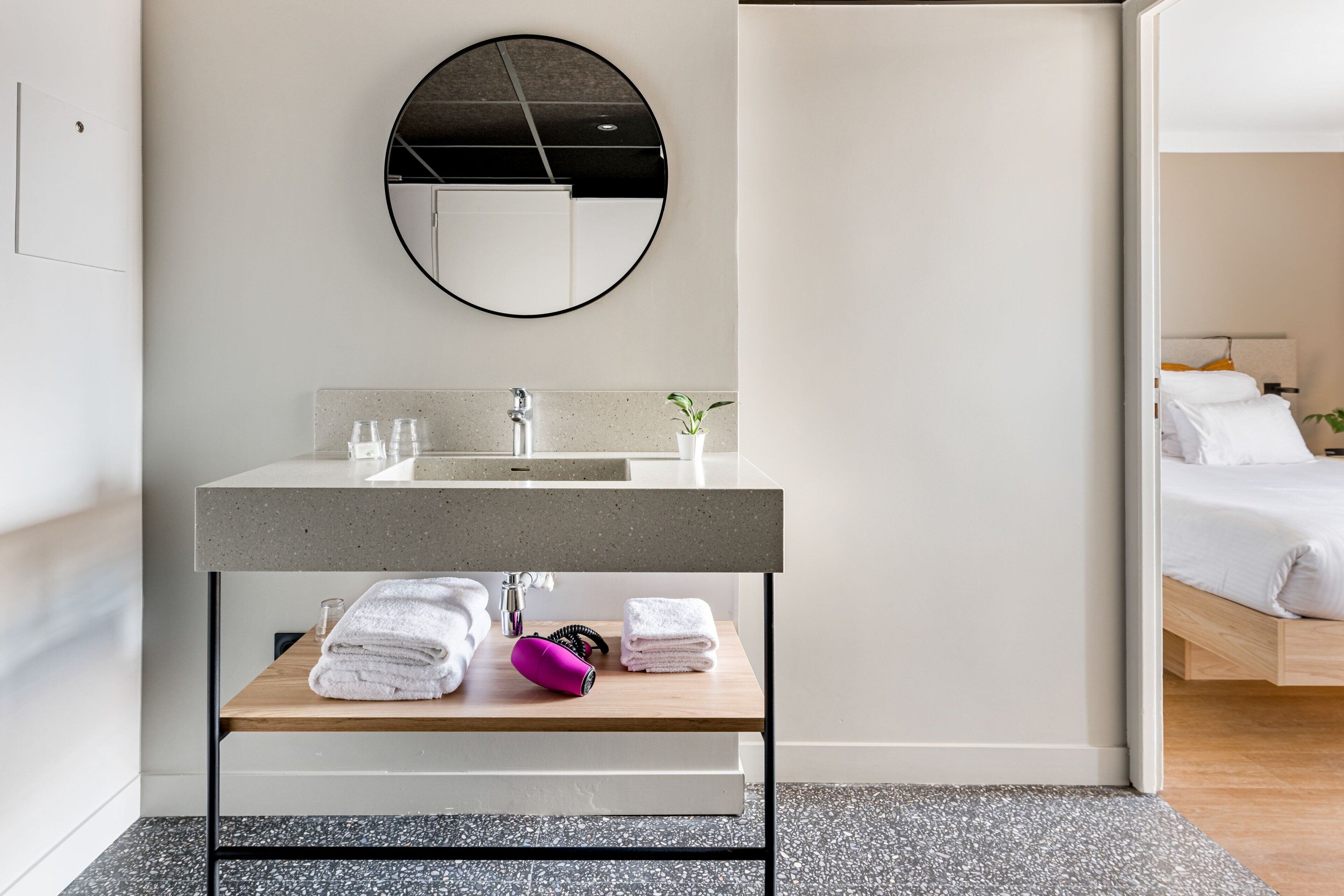 A modern bathroom with a round mirror, a sink, and a wooden shelf with towels.