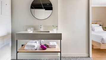 A modern bathroom with a round mirror, a sink, and a wooden shelf with towels.