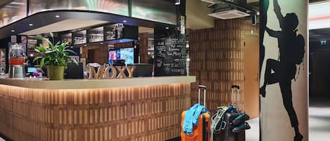 A reception area with a counter, a potted plant, and a wall with a silhouette of a person climbing. There are two suitcases and a backpack near the counter.