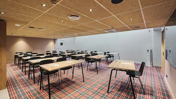 Un salón de conferencias con alfombra estampada, mesas de madera y sillas negras.