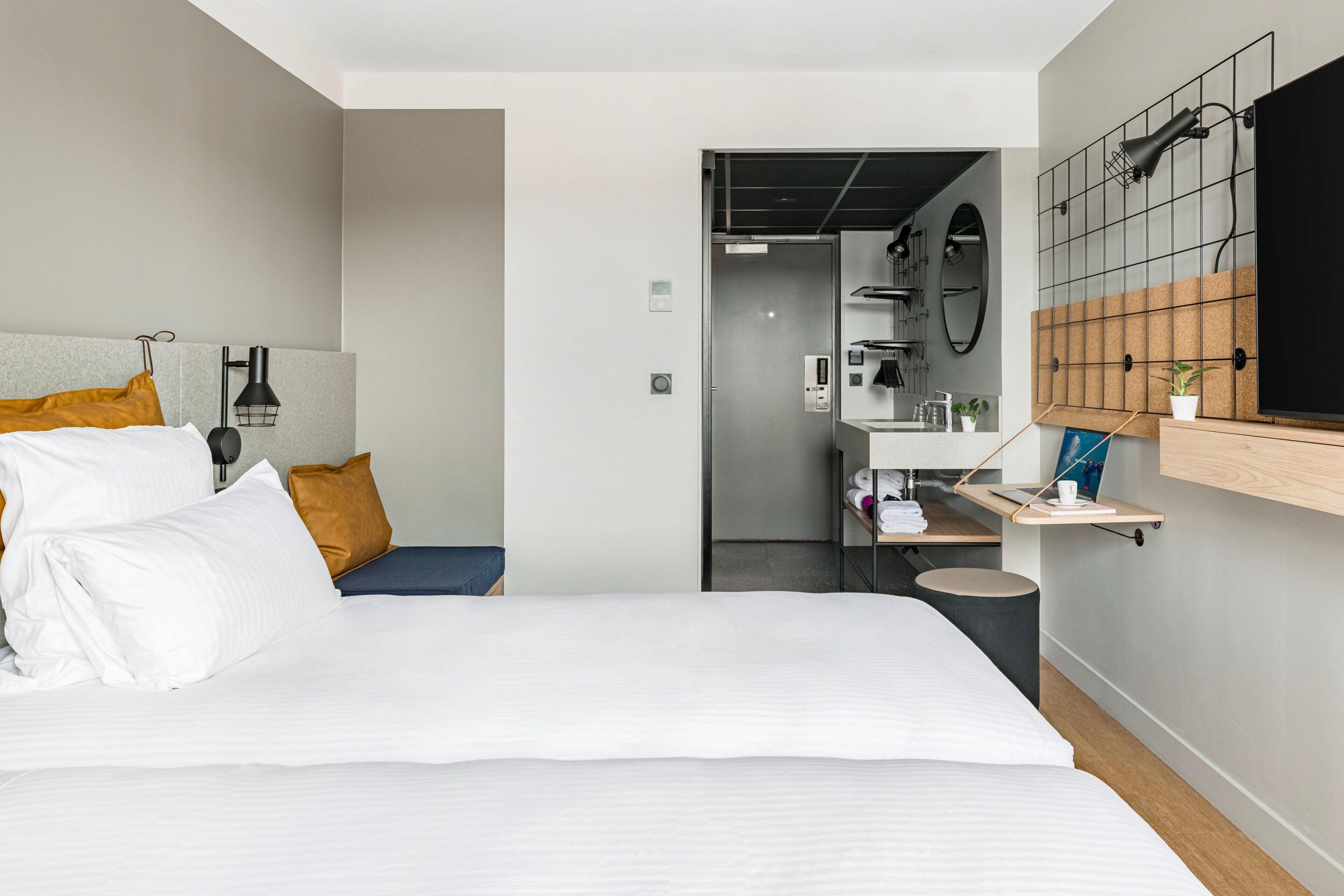 A modern hotel room with a large bed, a desk, and a bathroom visible through an open door.