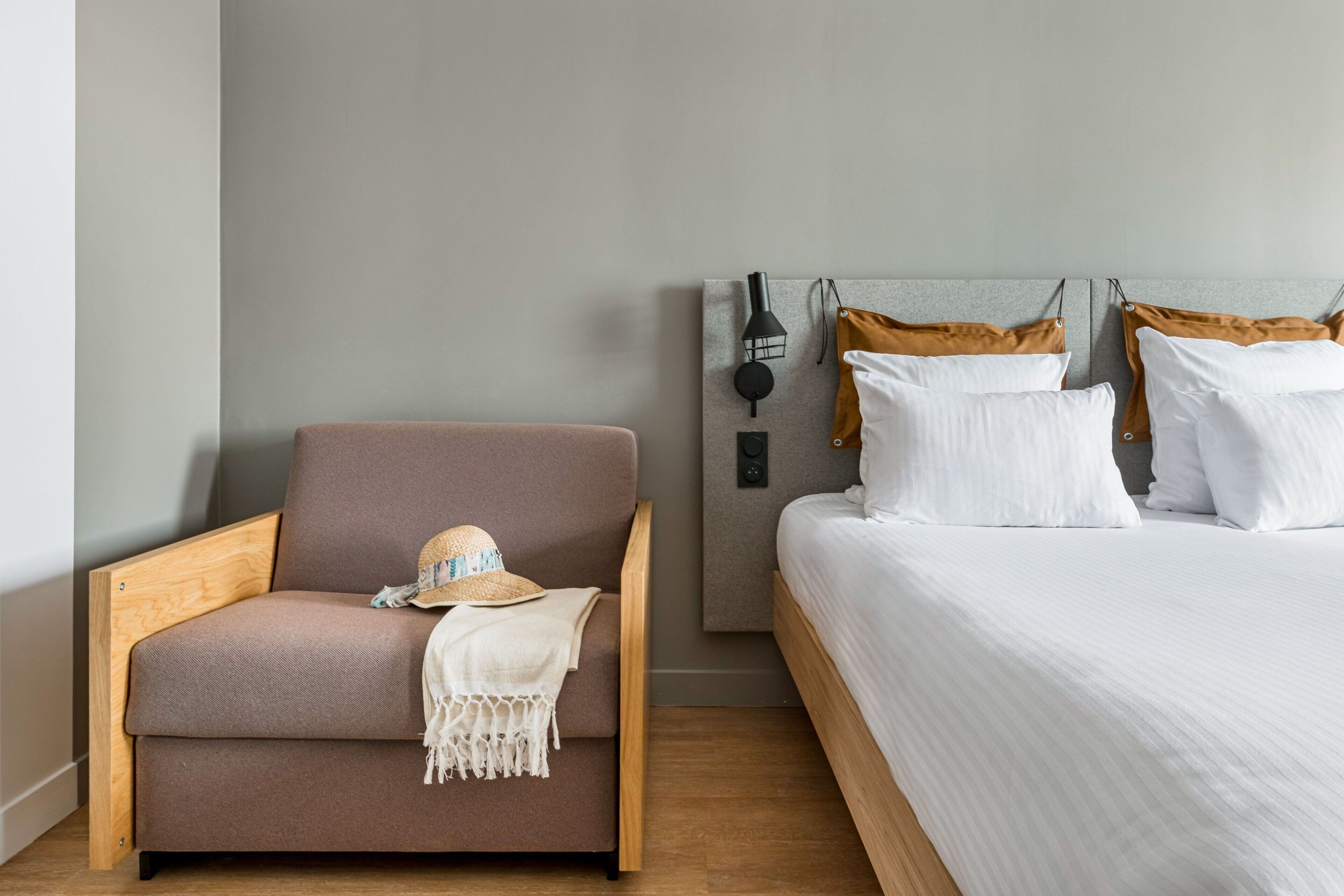 A bedroom with a bed, a wooden chair, a wall-mounted lamp, and a wall-mounted speaker.