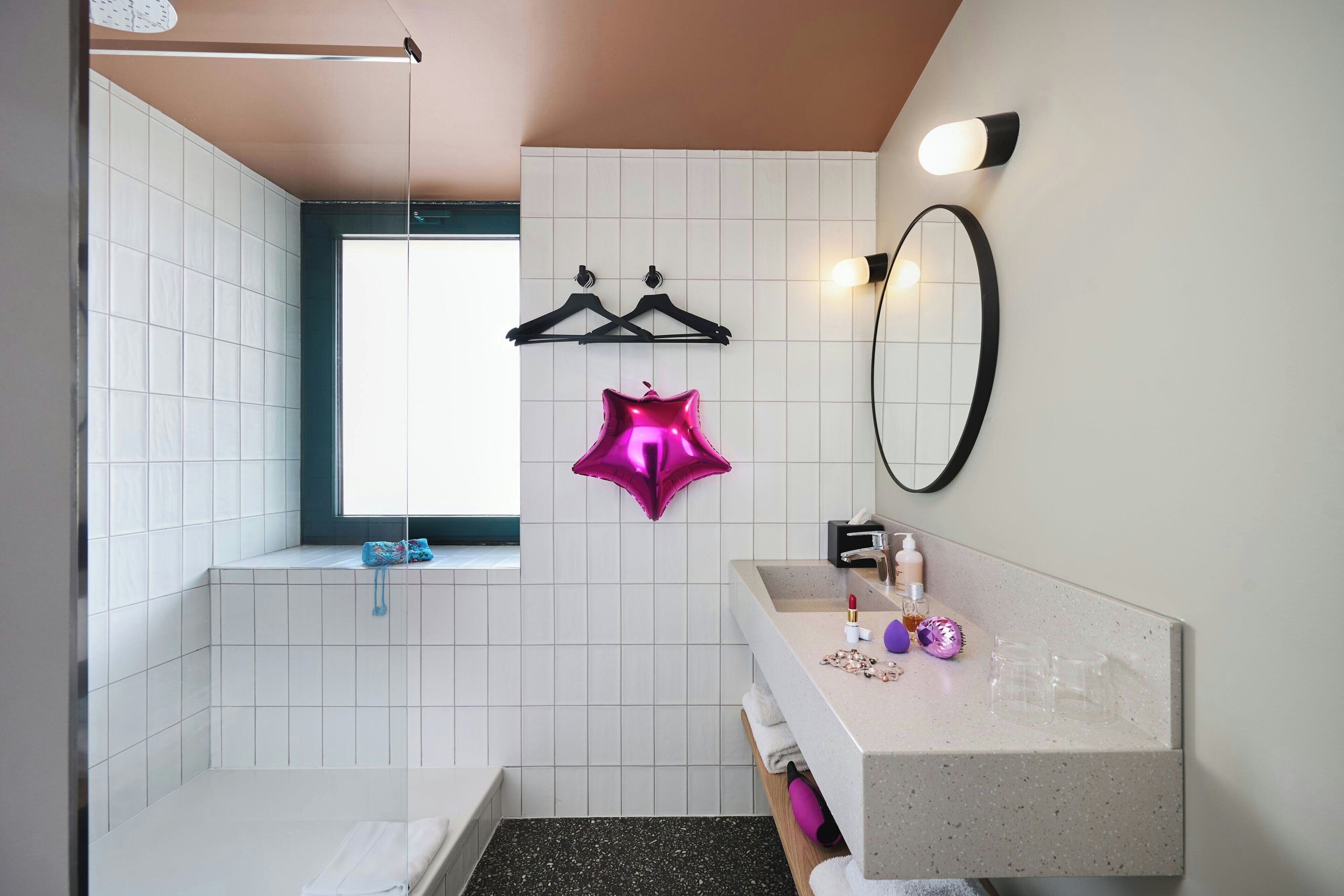 A bathroom with a bathtub, a sink with toiletries, a mirror, and a window.