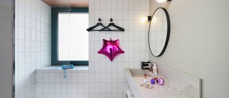 A bathroom with a bathtub, a sink with toiletries, a mirror, and a window.