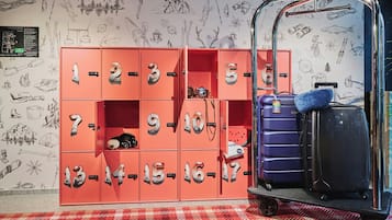 A set of numbered lockers with a camera inside one, a purple suitcase, and a cart with a blue bag.