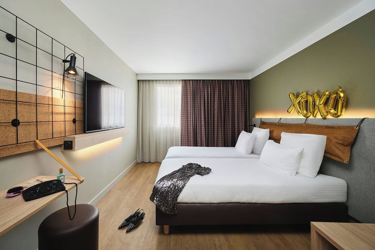 Une chambre d’hôtel avec un lit, une télévision, un bureau avec une lampe et une fenêtre avec des rideaux.